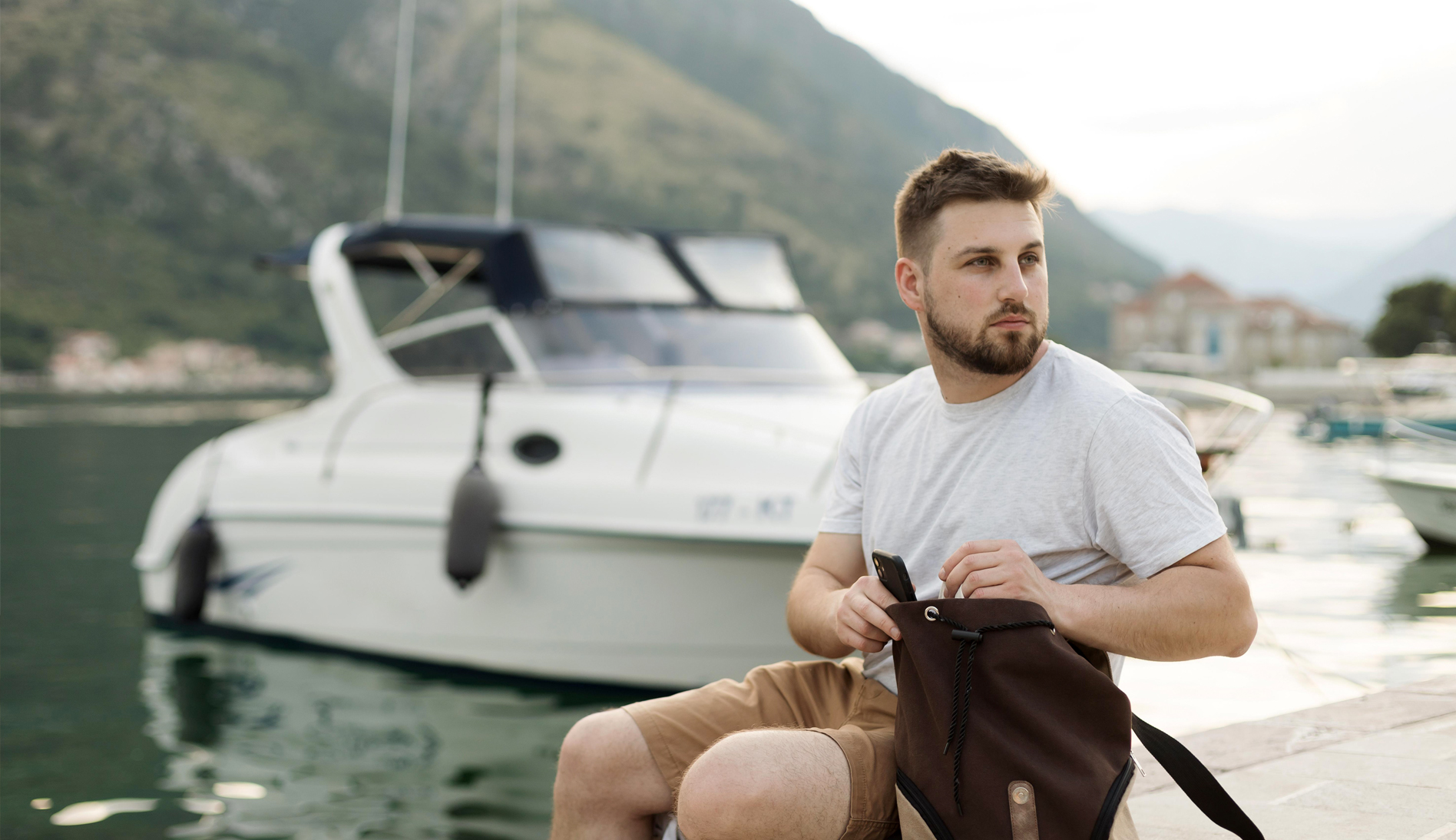 Hombre sentado junto a un yate en un puerto del Mediterráneo
